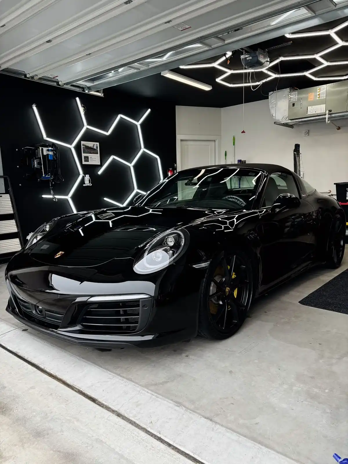 Black Porsche 911 gleaming under hexagon garage lights after a Masterpiece Detail