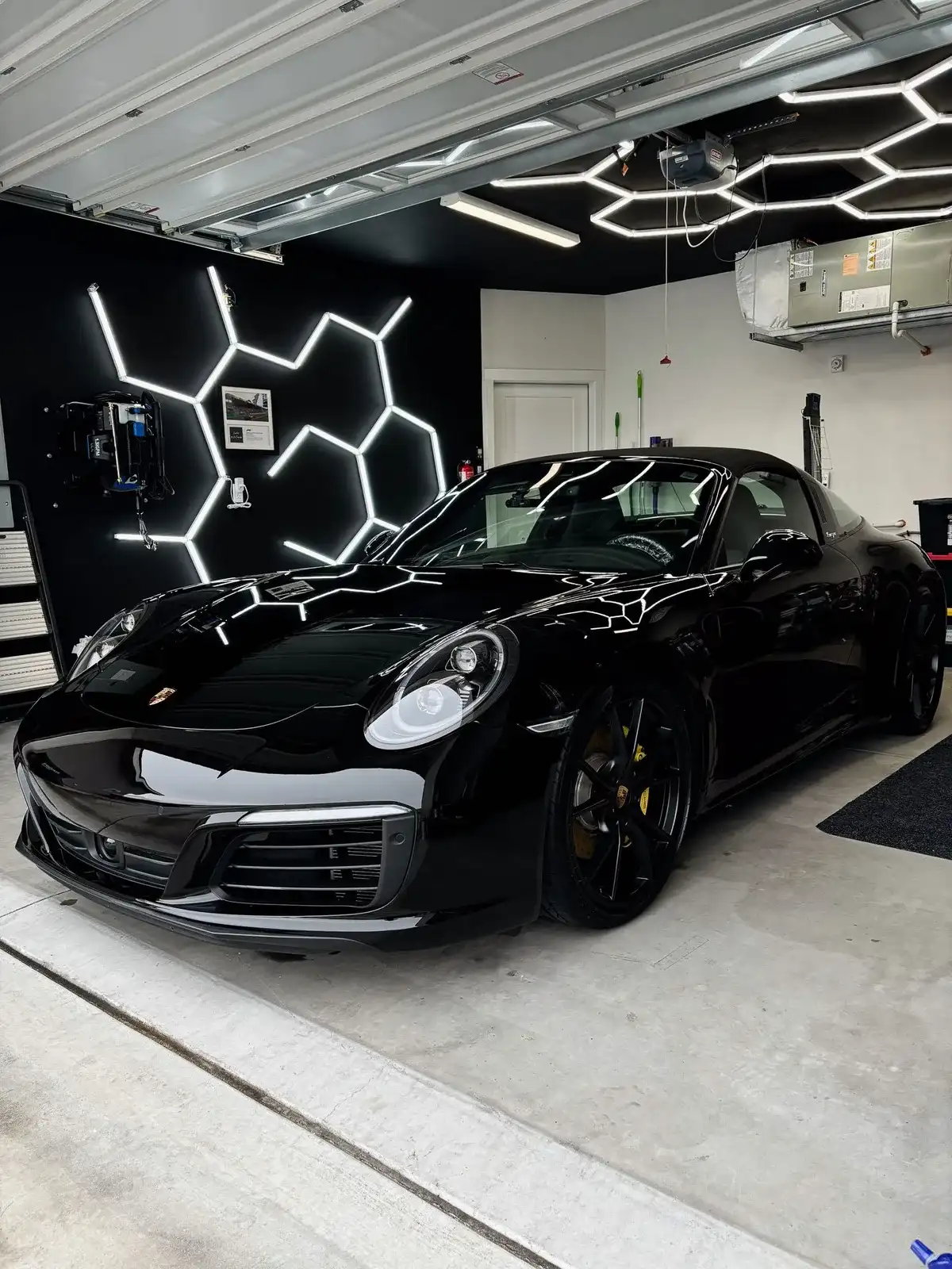 Black Porsche 911 gleaming under hexagon garage lights after a Masterpiece Detail
